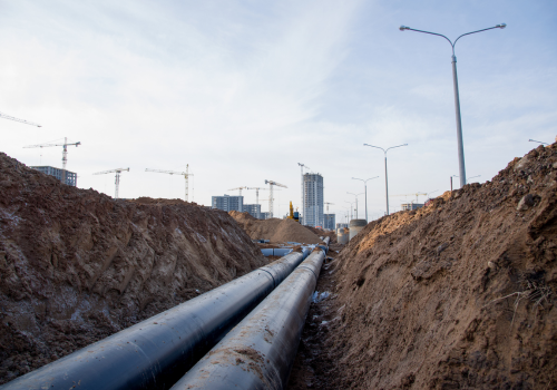 Laying of heating storm sewer pipes at the construction site. Installation of water main and sanitary sewer on background tower cranes and blue sky. Ground water drainage system pipes