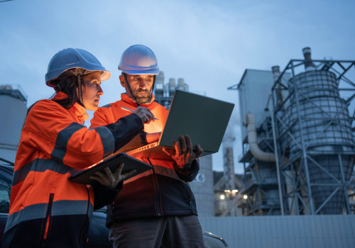 Man and woman working late with laptop in a power plant. Night shift.